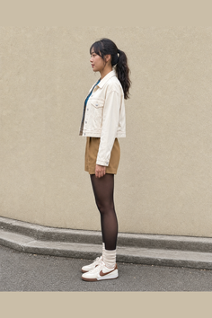 Woman in a cream denim jacket, shorts, and tights standing outdoors