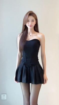 Woman with long hair wearing a black strapless dress and black tights indoors