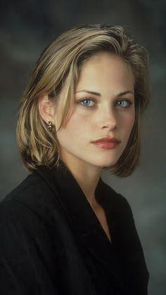 Woman with short blonde hair and blue eyes wearing a black jacket