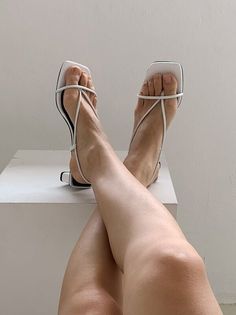 Person wearing white strappy sandals with crossed bare legs against a white background