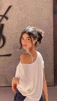 Woman with a messy bun and white t-shirt looking over her shoulder outdoors