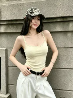 Woman with long hair and a camo cap wearing a spaghetti strap top and white pants