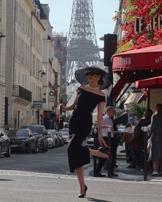 Woman in a black dress and wide brim hat posing on a city street with the Eiffel Tower in the background