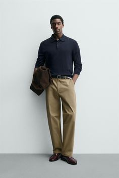 Man in a navy polo shirt and khaki pants holding a brown jacket