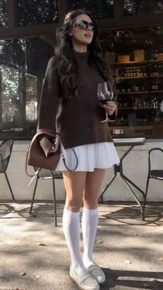 Woman in a brown sweater and white skirt holding a glass of red wine outdoors