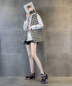 Person in a houndstooth vest and black shorts holding a magazine over their face