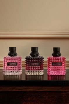 Three Valentino perfume bottles with studded caps on a dark wooden surface