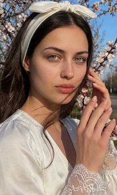 Woman with a white headband and green eyes holding a flowering branch