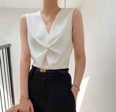 Woman in a white sleeveless top and black pants with a gold necklace