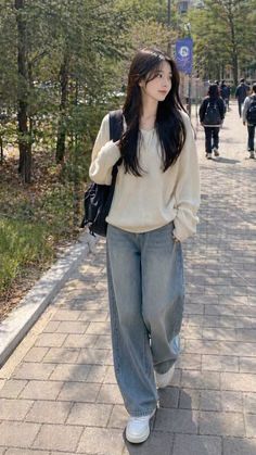 Woman with long dark hair wearing a loose sweater and wide leg jeans walking outdoors