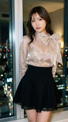 Woman in a sheer blouse with a bow collar and a black skirt by a window at night