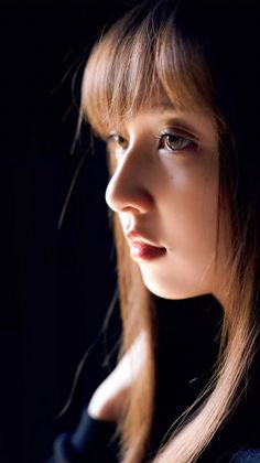 Close up portrait of a woman with long brown hair and bangs against a dark background