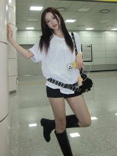 Woman in a white t-shirt and black shorts with long hair and earbuds indoors