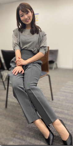 Woman with long hair wearing a grey top and pants, sitting indoors and smiling