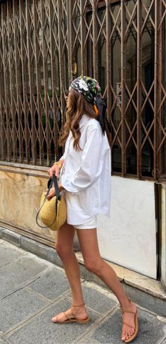 Woman in a white shirt and shorts with a floral scarf walking on a street