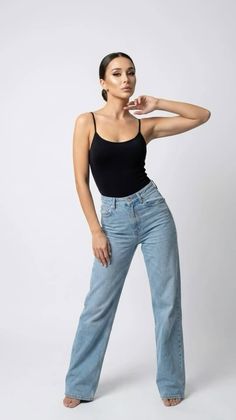 Woman in a black tank top and light wash jeans posing in a studio