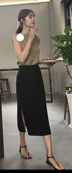 Woman in a sleeveless top and black slit skirt holding a tray indoors