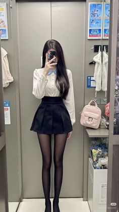 Woman in a white shirt and black pleated skirt taking a mirror selfie