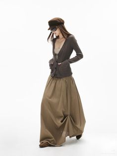 Woman in a brown cardigan, maxi skirt, and hat posing in a studio