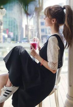 Woman with a ponytail in a black dress and white lace top, drinking indoors