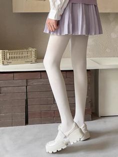 Person wearing a pleated skirt, white tights, and white shoes indoors