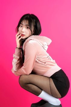 Woman in a pink hoodie and black shorts squatting against a pink background