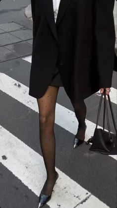 Person in a black blazer and polka dot tights walking on a crosswalk