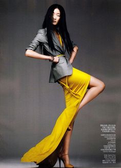 Woman in a yellow dress and gray blazer posing in a studio