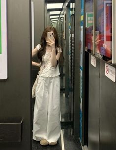 Woman in a white top and wide leg pants taking a mirror selfie in an elevator