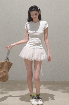 Woman in a white t-shirt and mini skirt holding a straw bag indoors