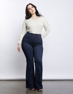 Woman with dark hair wearing a long sleeve shirt and flared jeans in a studio