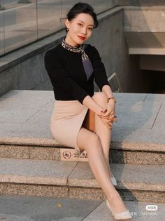 Woman in a black top and beige skirt sitting on outdoor stairs