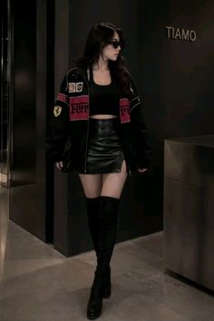 Woman in a black jacket, crop top, leather skirt, and thigh high boots indoors