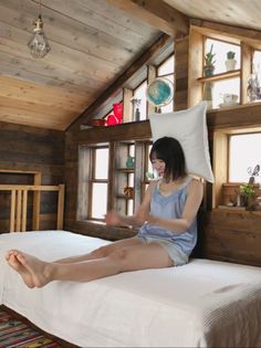Woman in a tank top and shorts sitting on a bed in a rustic wooden room