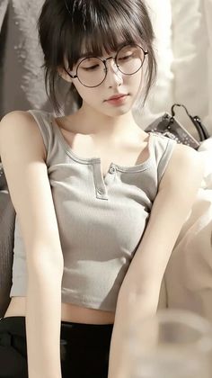 Woman with round glasses and a tank top in soft indoor lighting