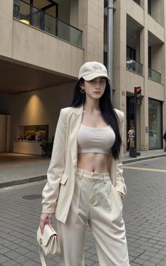 Woman in a crop top, blazer, and pants with a baseball cap on a street