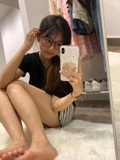 Young woman in glasses taking a mirror selfie while sitting on a white rug