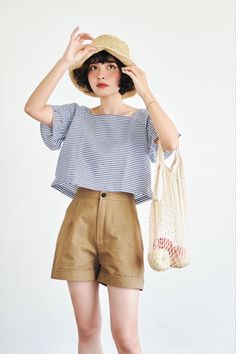 Woman in a straw hat, striped top, and brown shorts holding a mesh bag with apples