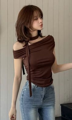 Woman with brown hair wearing an off-shoulder top and blue jeans indoors