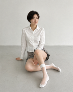 Woman with short hair in a white shirt and plaid skirt sitting on the floor