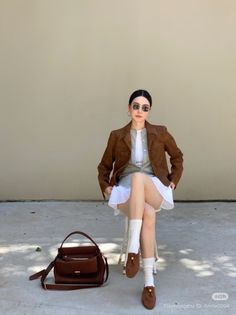 Woman in a brown jacket and white dress sitting outdoors