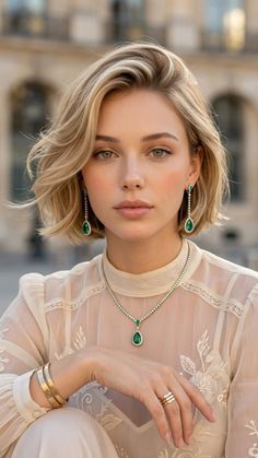 Woman with blonde hair wearing emerald jewelry and a sheer top outdoors