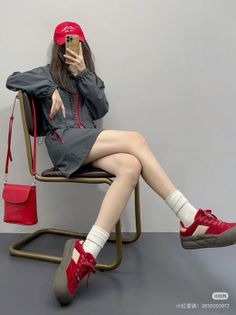 Person in a red cap and gray jacket sitting on a chair, taking a mirror selfie