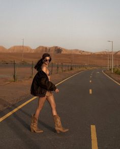 Woman in a bikini top and cowboy boots walking on a desert road