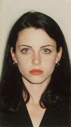 Woman with long black hair, blue eyes, and red lipstick wearing gold hoop earrings