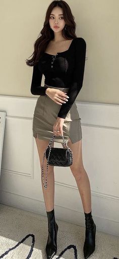 Woman in a black long-sleeve top and mini skirt holding a quilted bag
