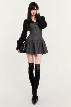Woman in a pinstripe dress, black blouse, and lace stockings posing on a white background
