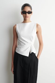 Woman in a white top and black pants wearing sunglasses in a studio