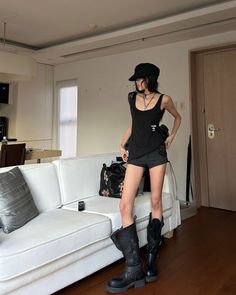 Woman in a black tank top, shorts, and boots standing indoors