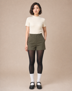 Woman with short hair wearing a ribbed top, olive shorts, and black tights